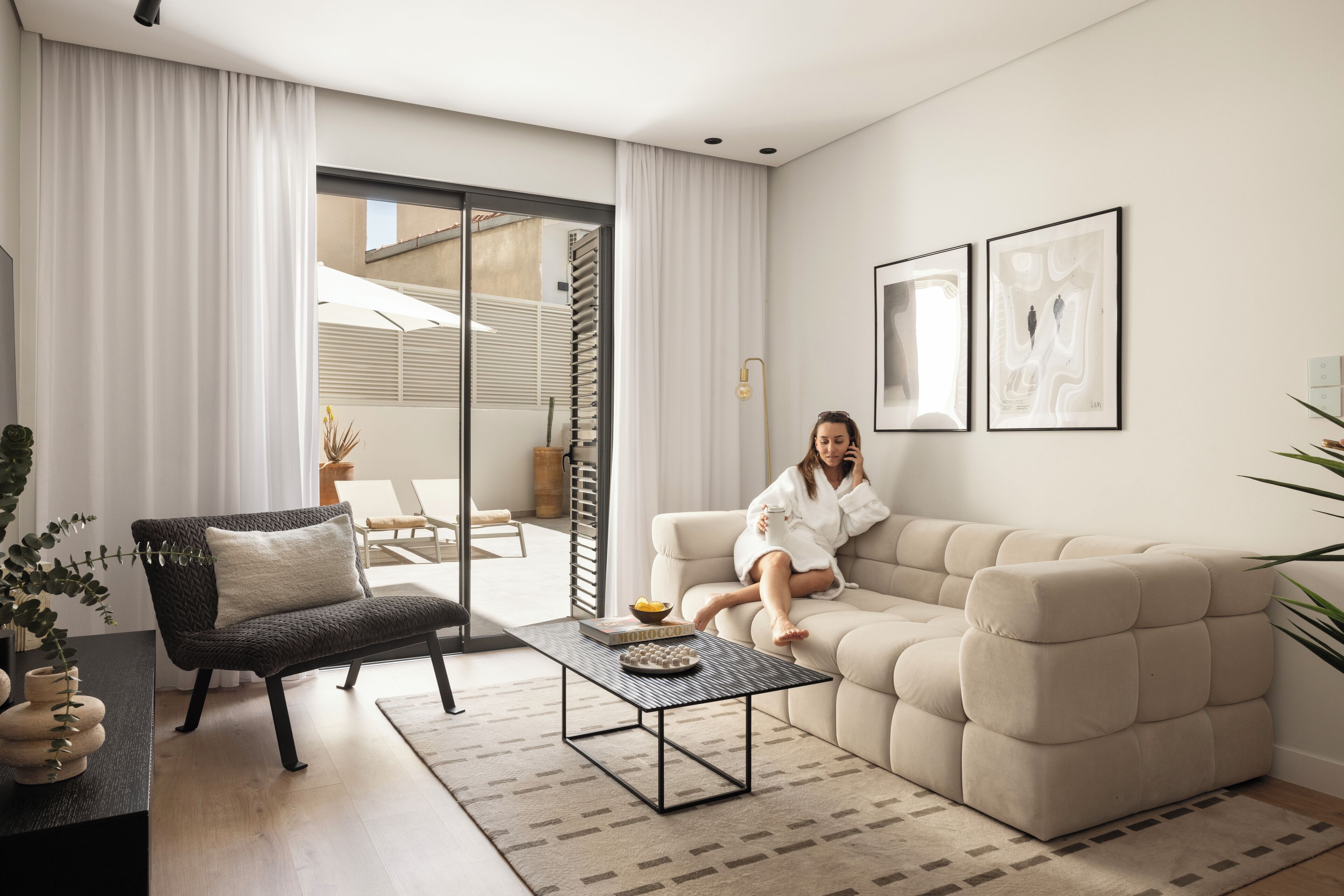 A modern living room with a sofa, a coffee table, and a chair. There is a sliding glass door leading to an outdoor area.