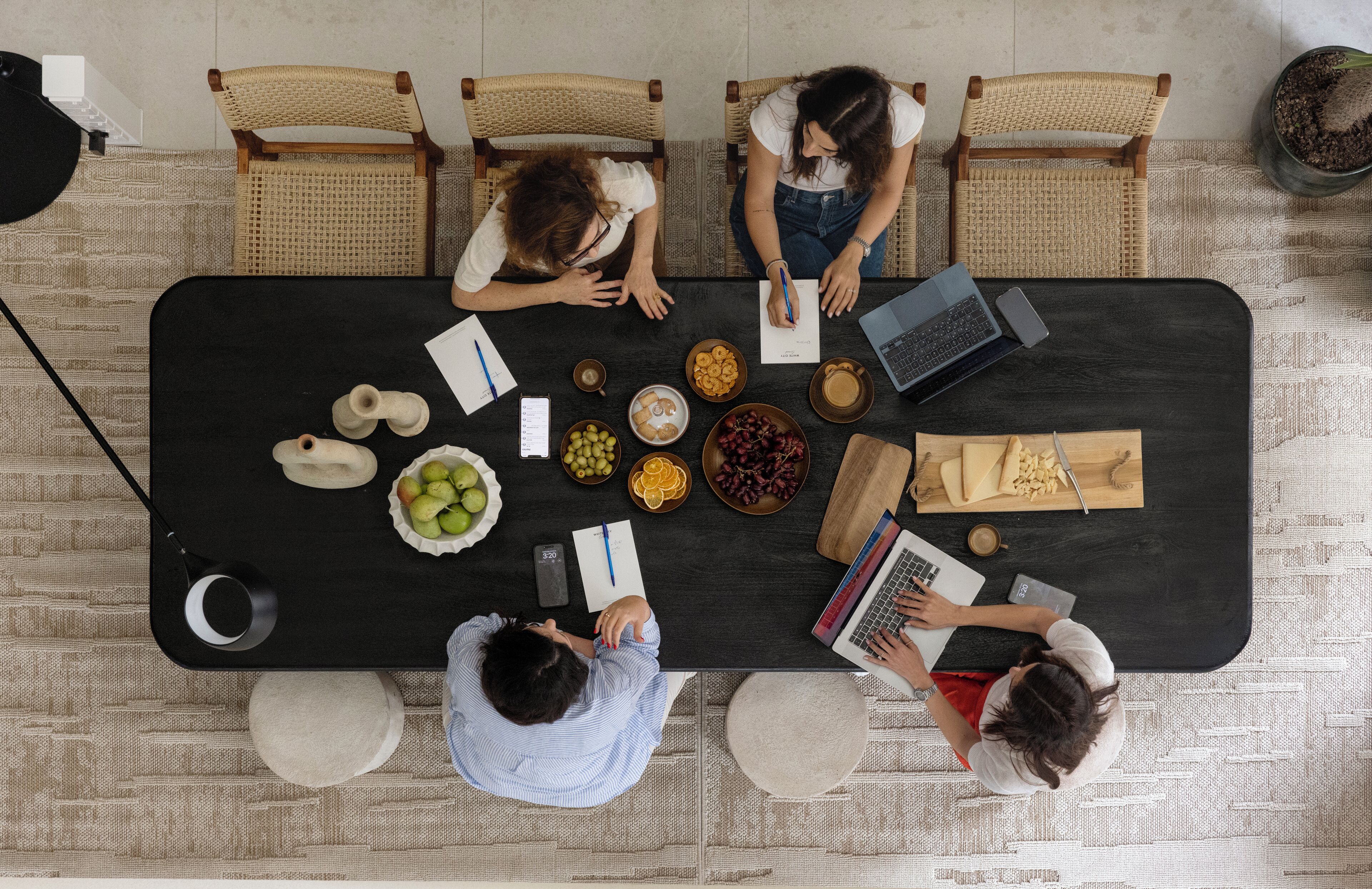 Vue d’ensemble d’une table à manger où sont assis quatre personnes, avec des ordinateurs portables et divers plats.