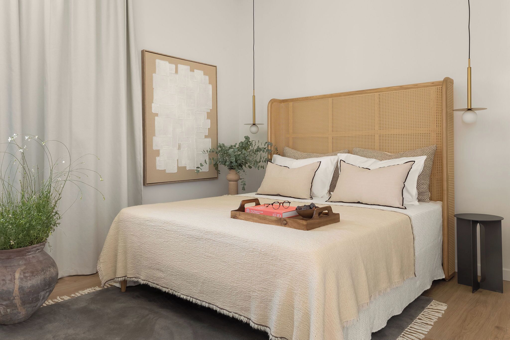 A neatly made bed with a woven headboard, a bedside table, a potted plant, and a framed artwork on the wall.