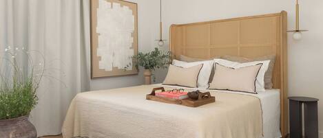 A neatly made bed with a woven headboard, a bedside table, a potted plant, and a framed artwork on the wall.