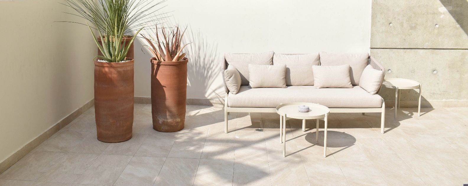 Et moderne udendørs opholdsområde med en sofa og et lille bord, omgivet af terrakotta krukker med planter.