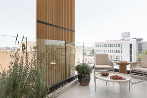 Un balcone moderno con parete in legno, ringhiera in vetro e zona salotto con tavolo e sedie.