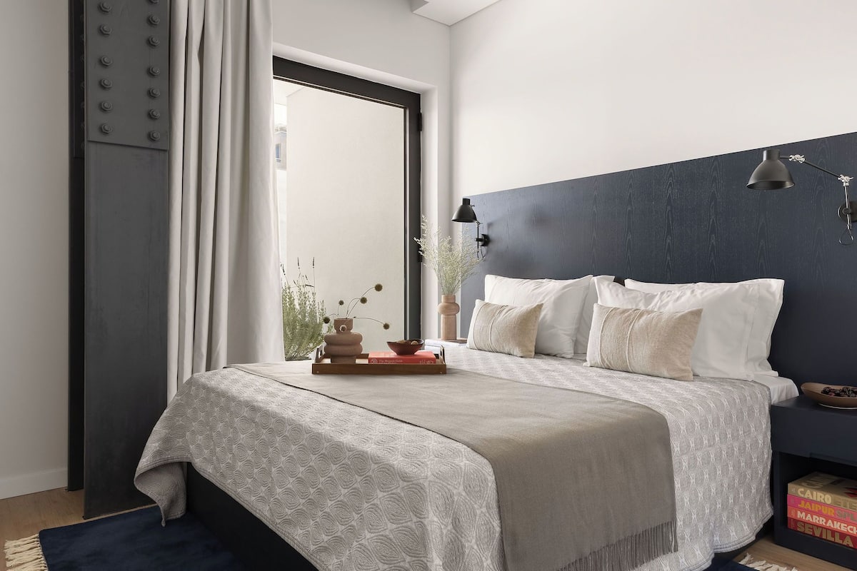 Een slaapkamer met een bed, nachtkastje, lamp en raam met gordijnen.