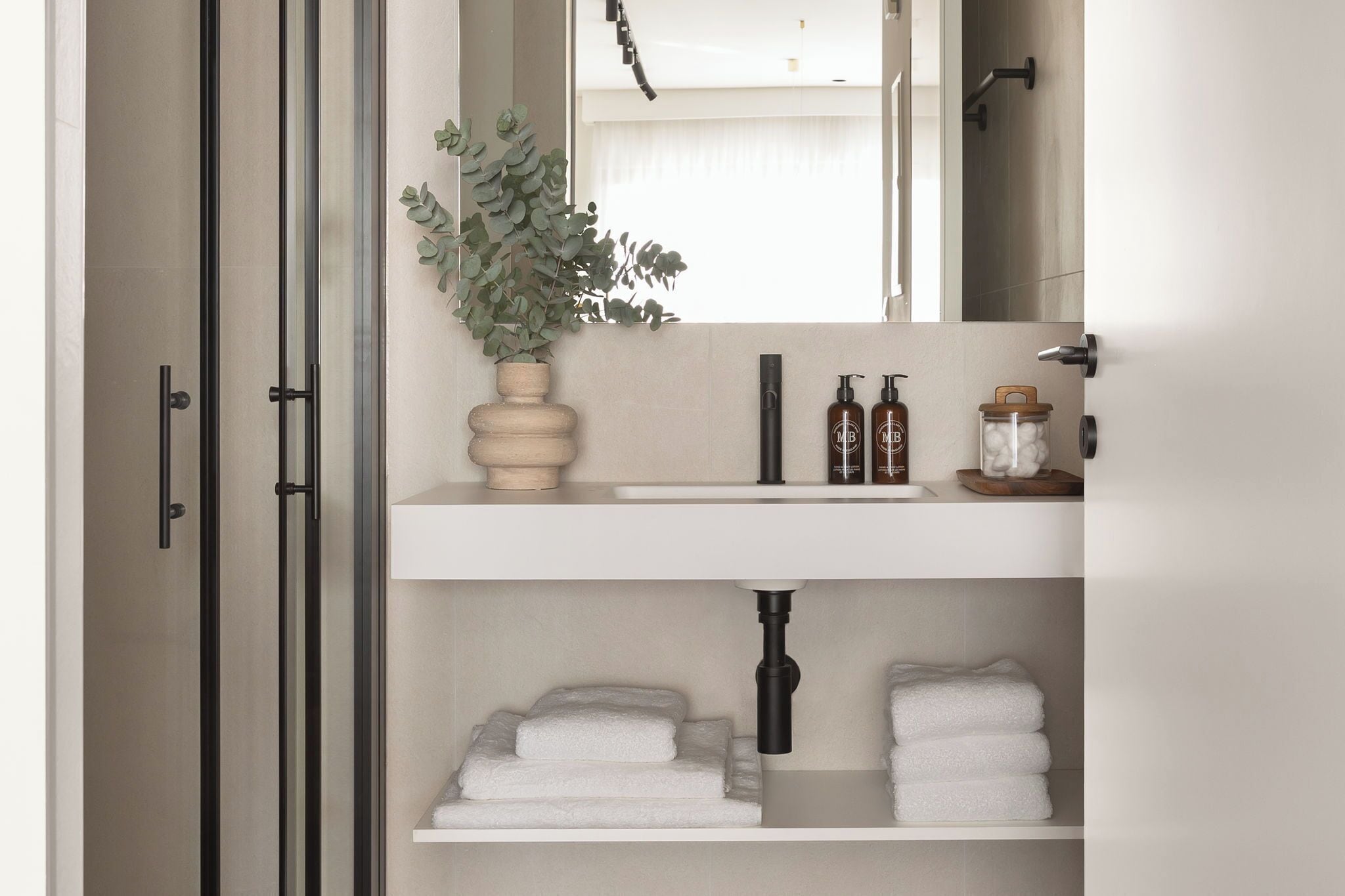 Une salle de bain avec un lavabo blanc, un miroir, une plante en pot et des serviettes soigneusement pliées.