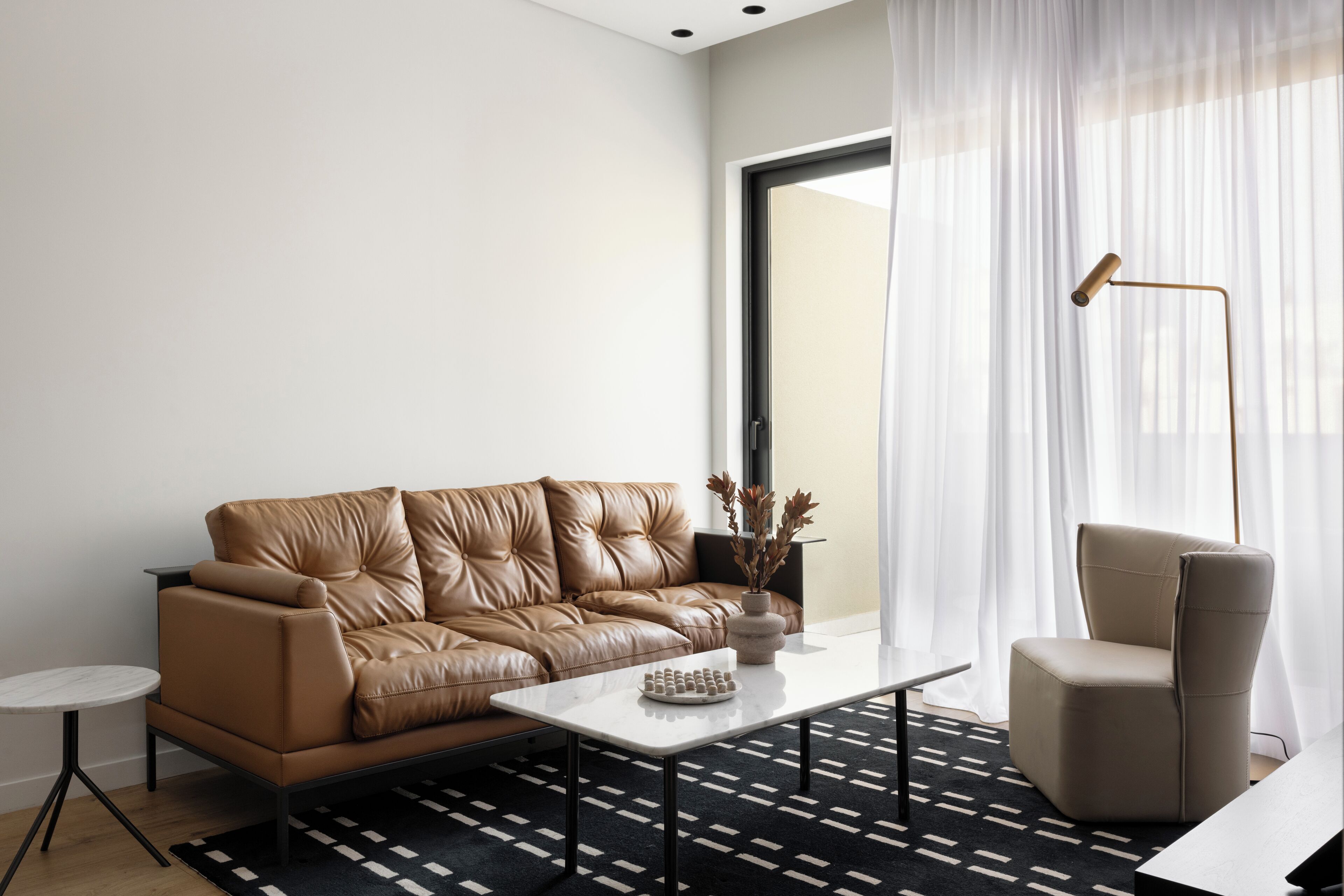 A modern living room with a brown leather sofa, a white coffee table, a side table, and a floor lamp.