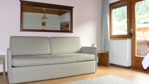 Een woonkamer met een bank, een tafeltje, een spiegel en een raam met uitzicht op bomen.
