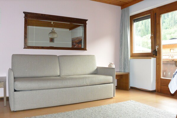 A living room with a sofa, a small table, a mirror, and a window with a view of trees.