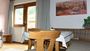 Een knus ingerichte kamer met een houten stoel, een bed, een tafel met tafelkleed en een schilderij aan de muur.