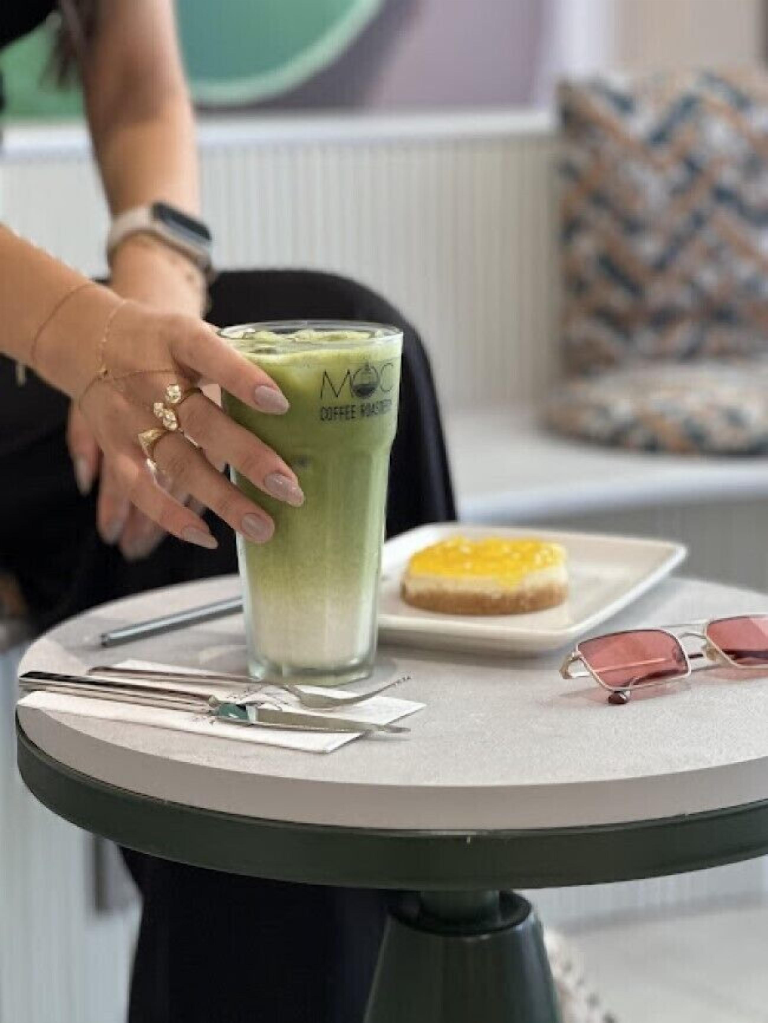 A table with a glass of green beverage, a plate with a pastry, and a pair of sunglasses.