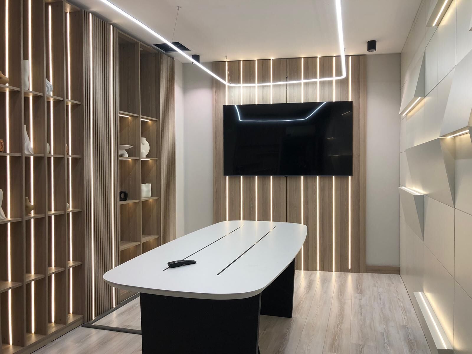 Habitació moderna amb una taula blanca, televisió de pantalla plana penjada a la paret i prestatges integrats amb il·luminació.