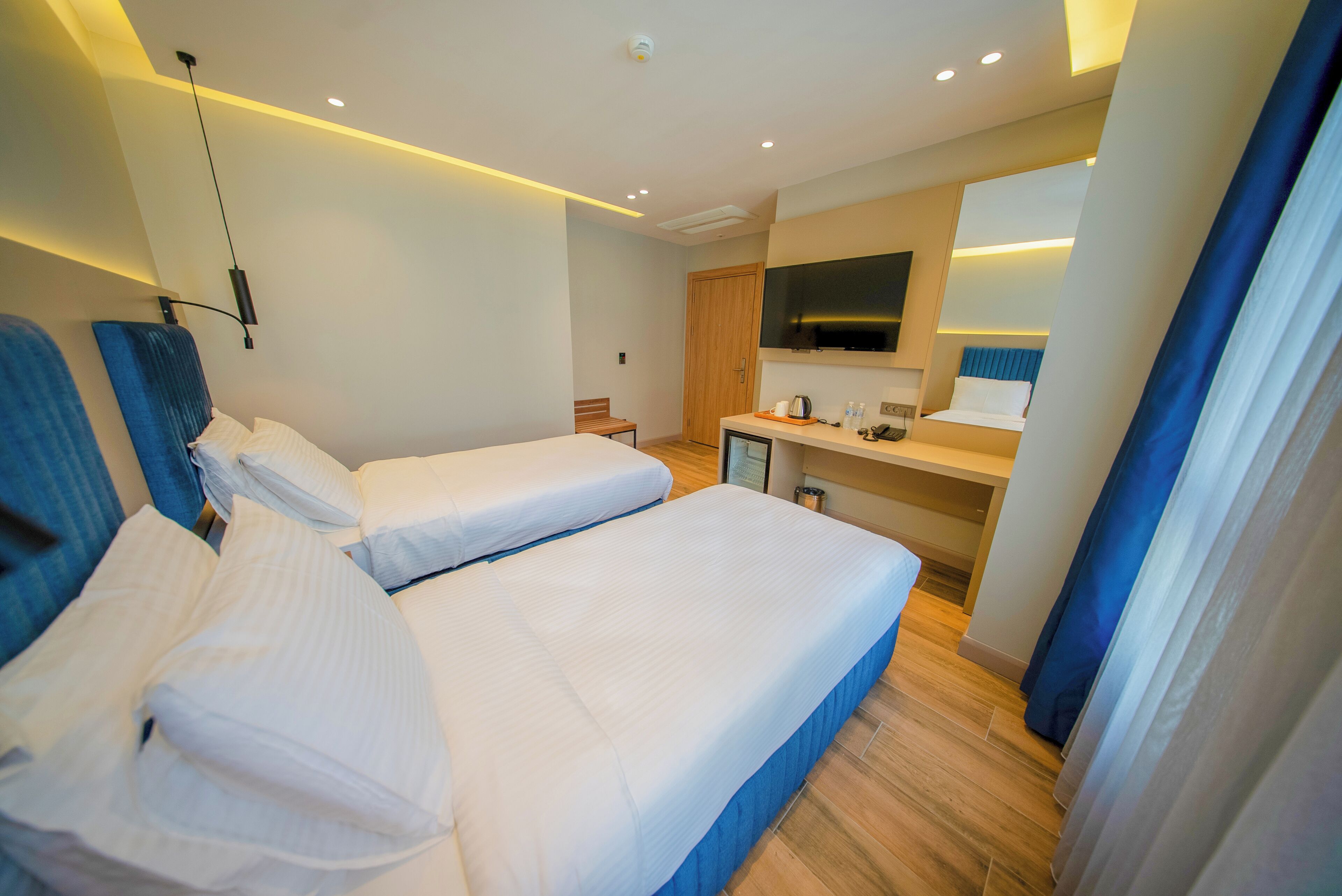A hotel room with two beds, a small kitchenette, a TV, and a bathroom.