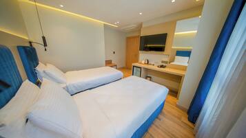 A hotel room with two beds, a small kitchenette, a TV, and a bathroom.
