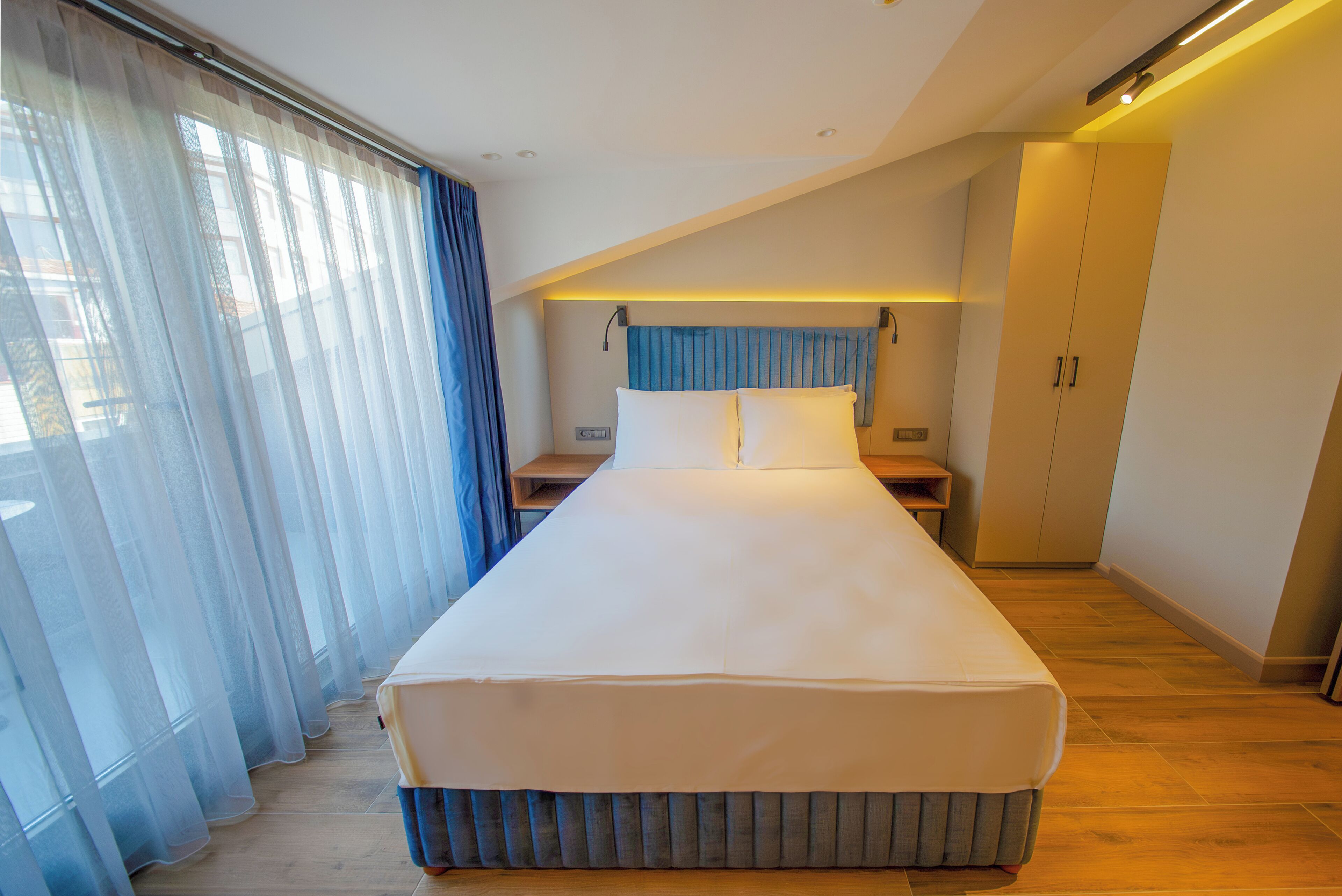 A modern bedroom with a large bed, a bedside table, a nightstand, and a wardrobe.