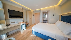 A modern hotel room with a large bed, a flat-screen TV mounted on the wall, a small desk with a chair, and a bathroom with a mirror and sink. - The Palm Bosphorus Hotel (Istanbul)