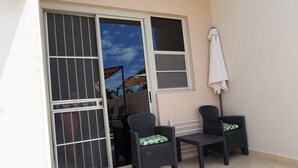 Un balcone con due poltrone in vimini, un tavolino e un ombrellone bianco.