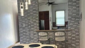 Zona pranzo con tavolo e sedie, ventilatore a soffitto e angolo cottura sullo sfondo.