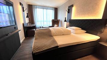 A modern hotel room with a large bed, a desk, a chair, and a TV on the wall.