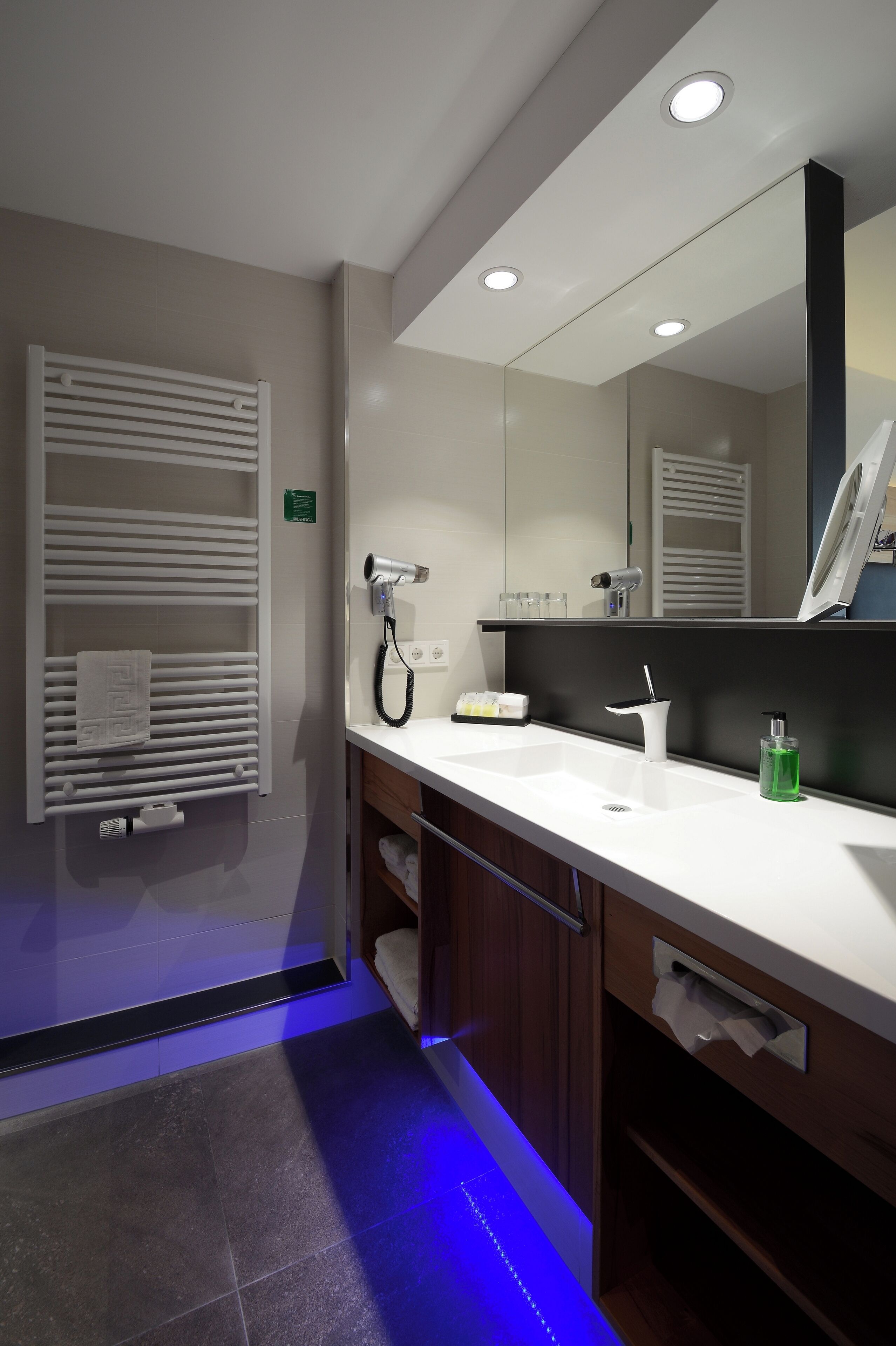 A modern bathroom with a white sink, a mirror, a towel rack, and a heated towel rail.