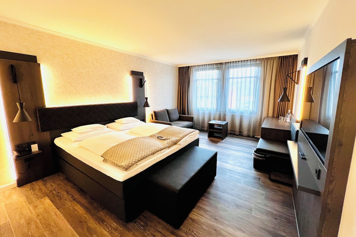 A hotel room with a large bed, a bedside table, a desk, a chair, and a TV.