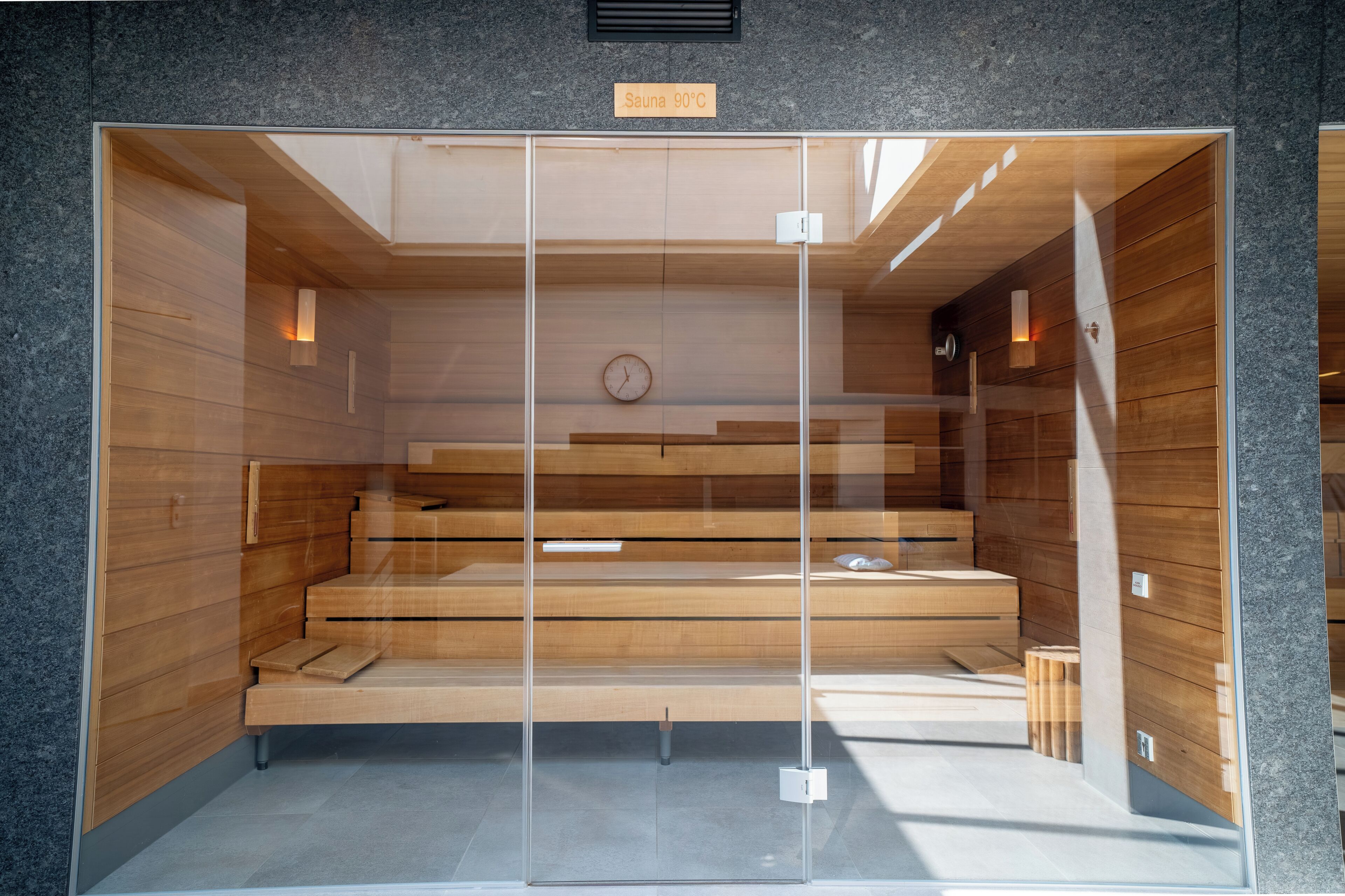 A sauna with a wooden interior, a clock, and a sign indicating 90°C temperature.