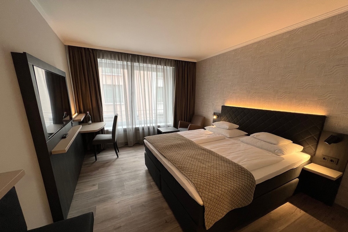 A hotel room with a large bed, a desk, a chair, and a TV.