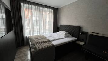 Une chambre d’hôtel moderne équipée d’un lit, d’une table de chevet, d’une télévision et d’une fenêtre avec des rideaux.