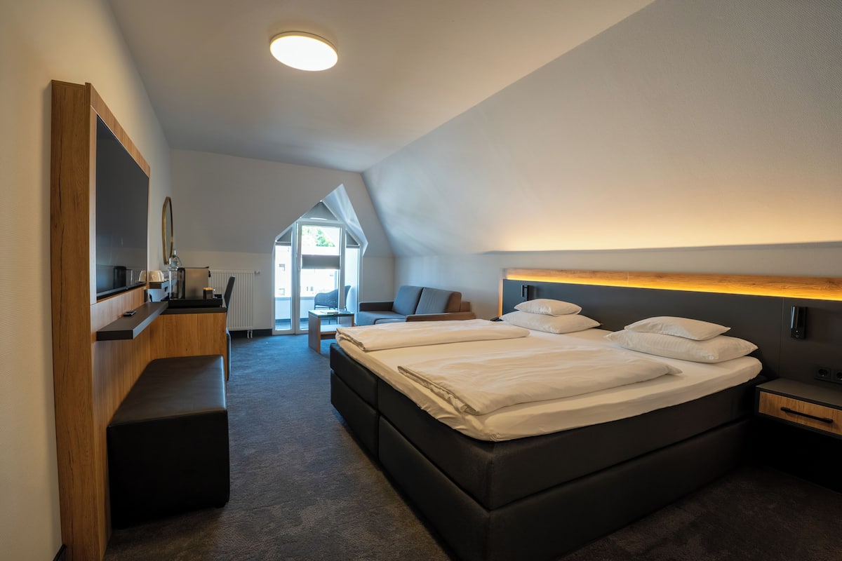 A modern hotel room with a large bed, a desk, and a mirror.