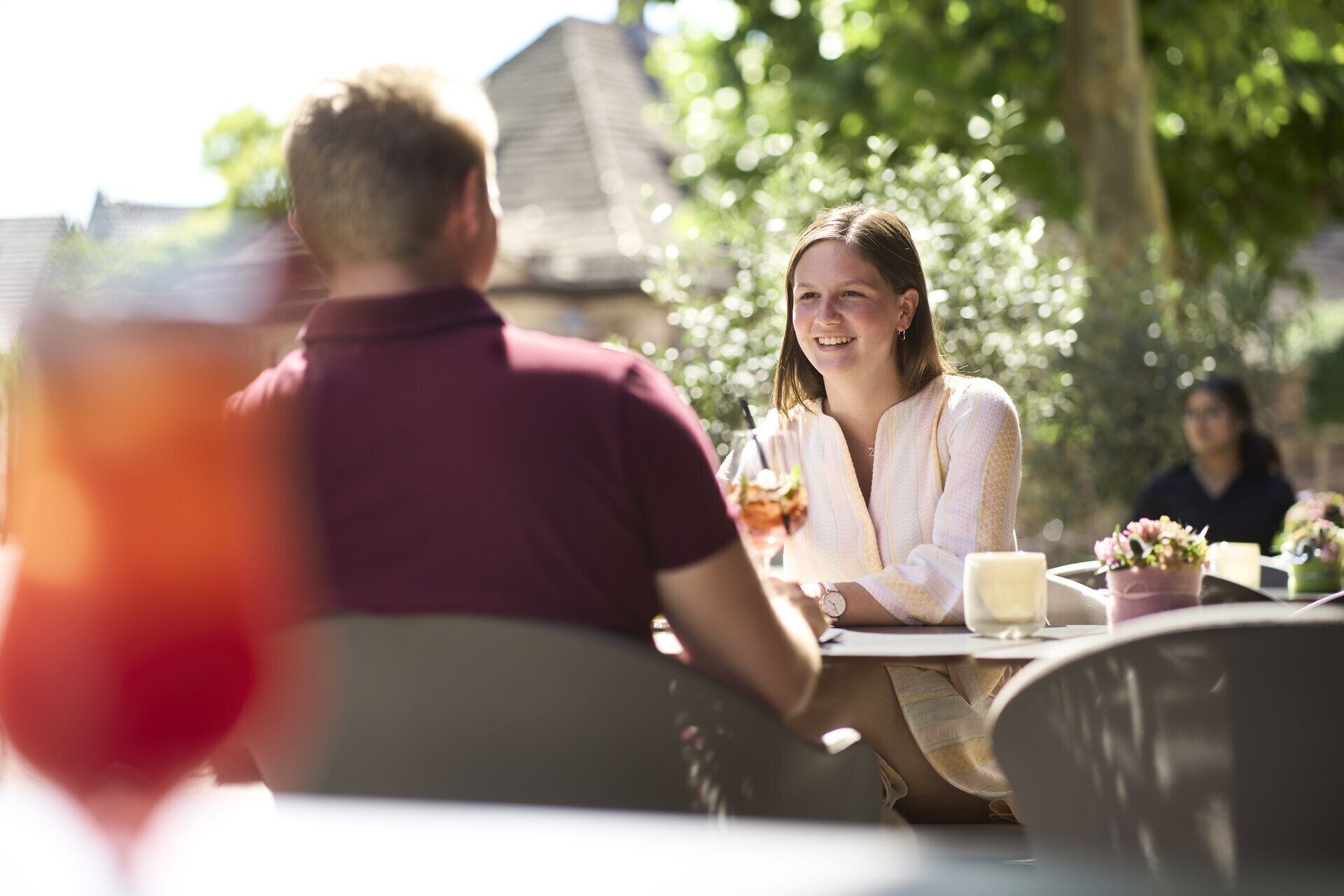A couple dining outdoors with a table, chairs, and a glass of drink.