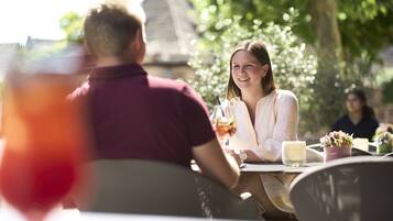 A couple dining outdoors with a table, chairs, and a glass of drink.
