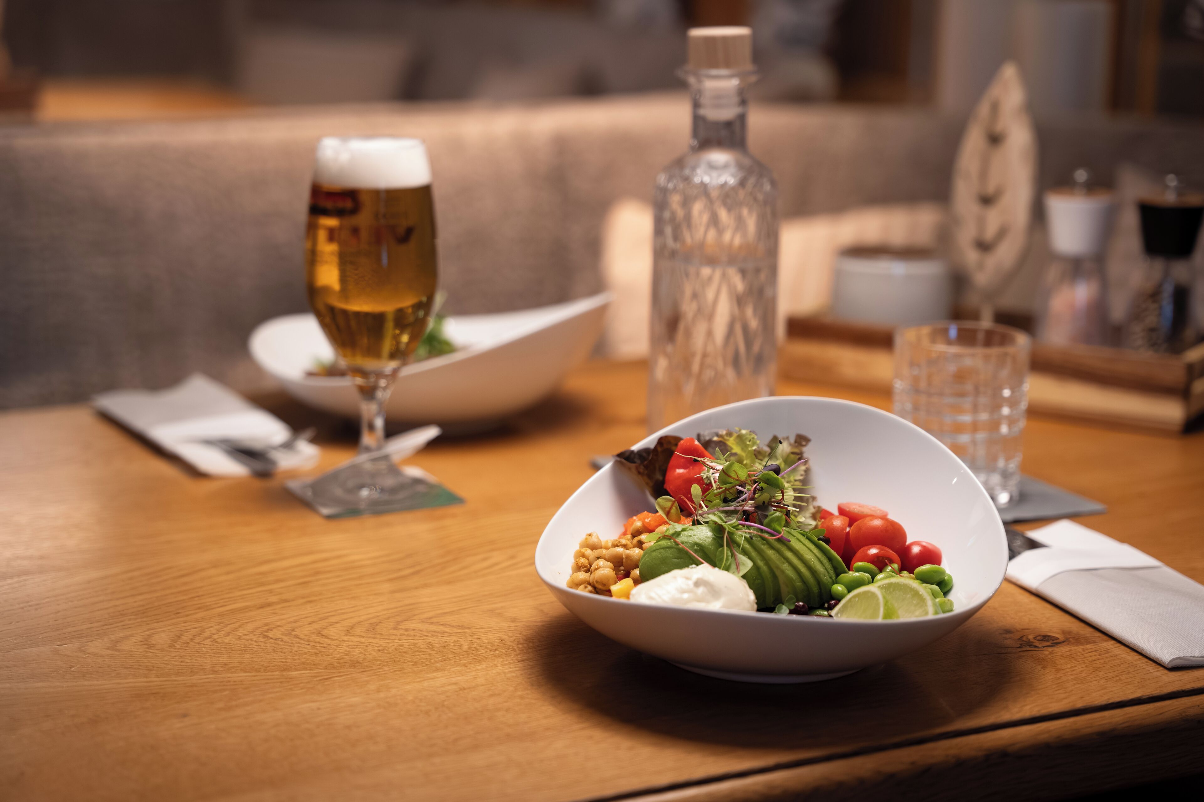 A dining table with a bowl of salad, a glass of beer, and a bottle of water.