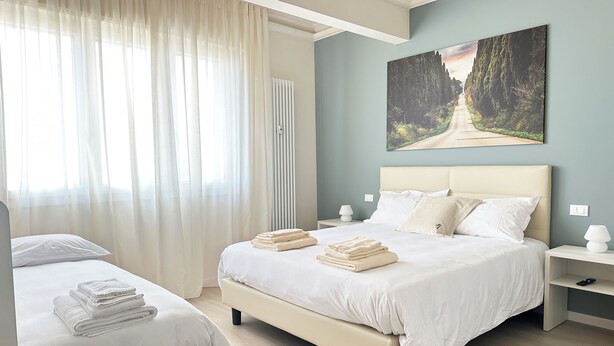 A hotel room with a large bed, a smaller bed, a bedside table with a lamp, and a painting on the wall. - Toscana da aMare (Cecina)