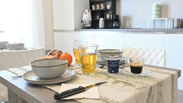 Un tavolo da pranzo con una ciotola, un coltello, un bicchiere di tè, un bicchiere di caffè e una tazza di latte.
