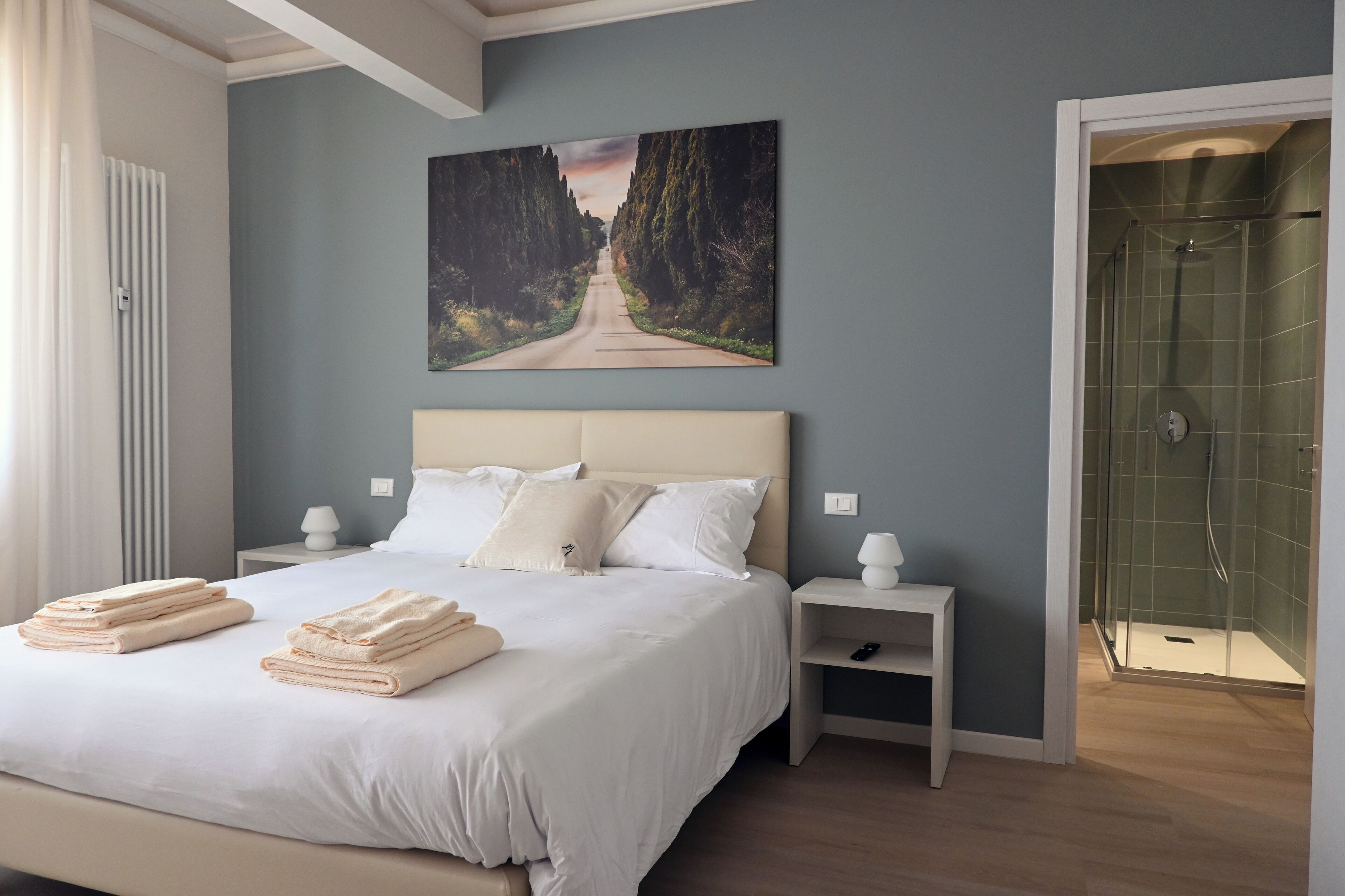 A bedroom with a large bed, a nightstand, a painting on the wall, and a shower area.
