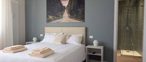 A bedroom with a large bed, a nightstand, a painting on the wall, and a shower area.