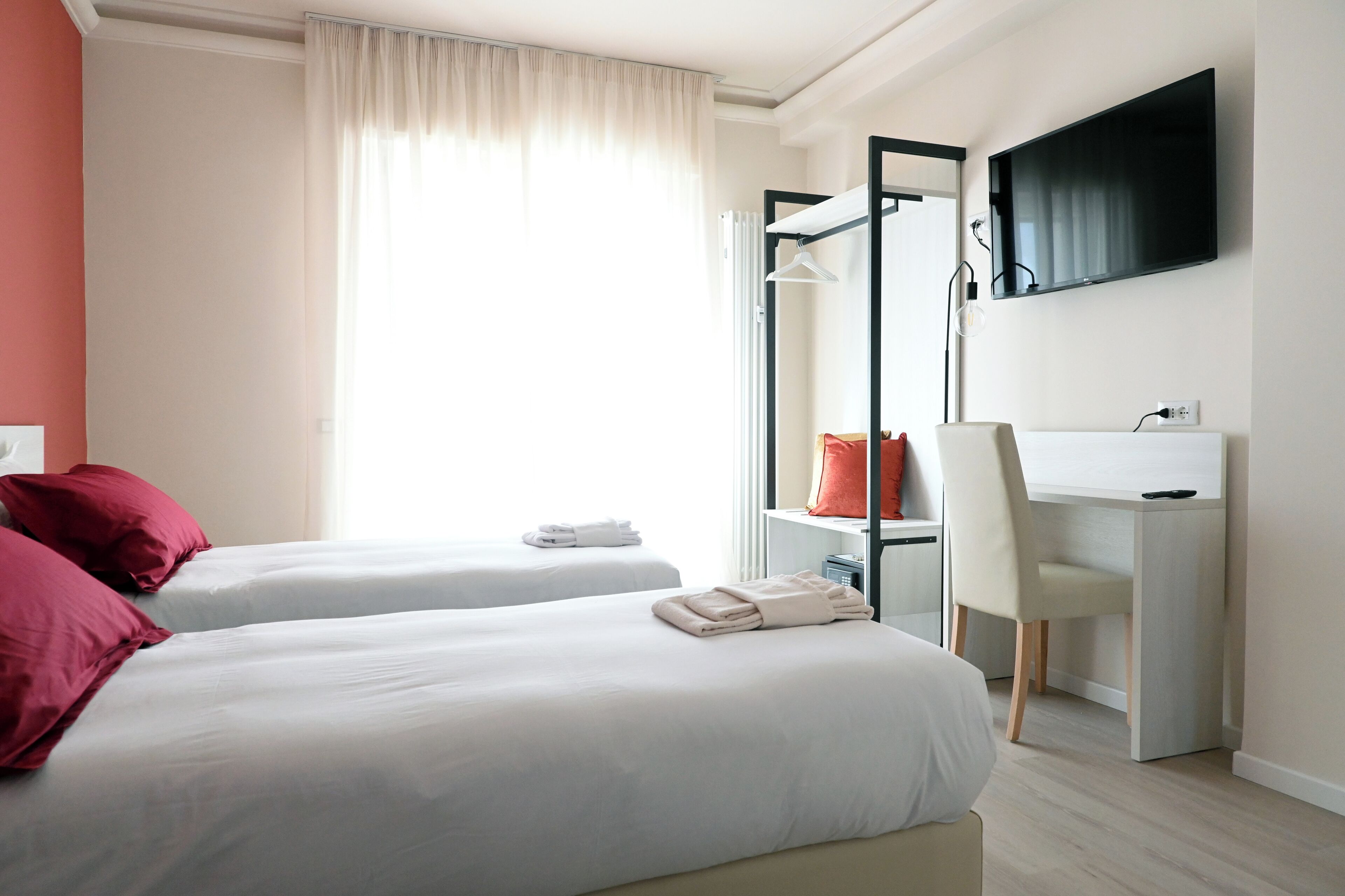 Habitación de hotel con dos camas, un escritorio, una silla, un televisor y una ventana con cortinas.