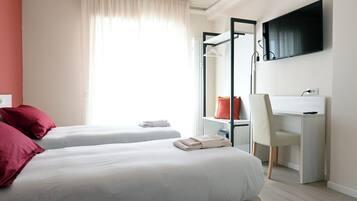 Habitación de hotel con dos camas, un escritorio, una silla, un televisor y una ventana con cortinas.