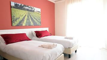 Quarto de hotel com duas camas, almofadas vermelhas, um quadro de paisagem grande na parede e uma janela com cortinas.
