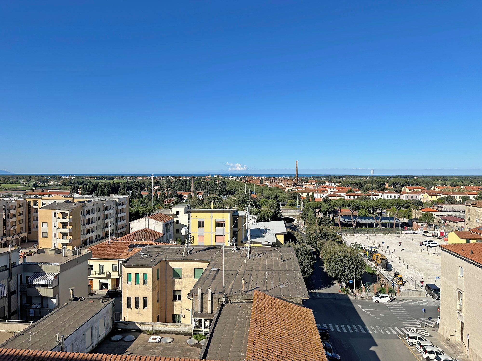 Un paysage urbain mêlant bâtiments résidentiels et commerciaux, un ciel bleu dégagé et une vue lointaine sur la mer.