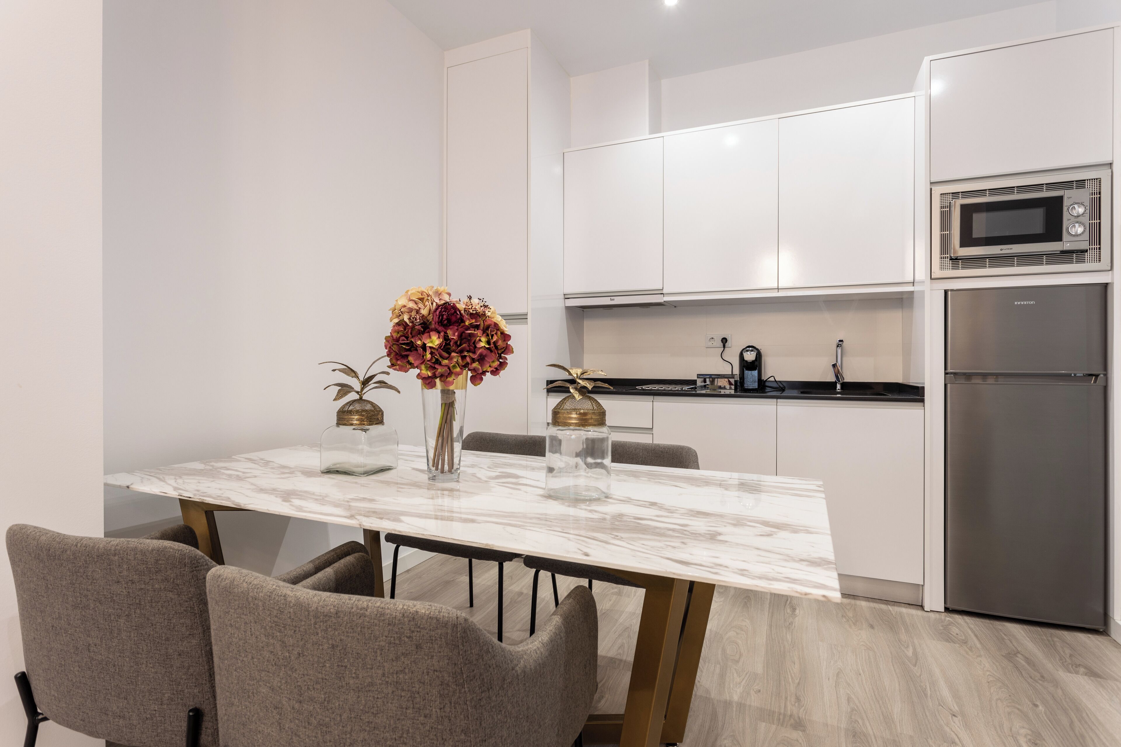 A modern kitchen with white cabinets, a stainless steel refrigerator, and a microwave.