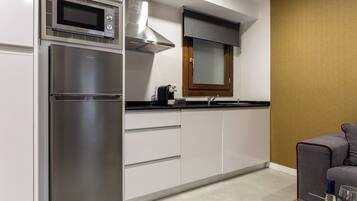 Cocina compacta con microondas integrado, horno y cocina a gas. Hay una ventana con persiana, un lavamanos y una pequeña encimera.