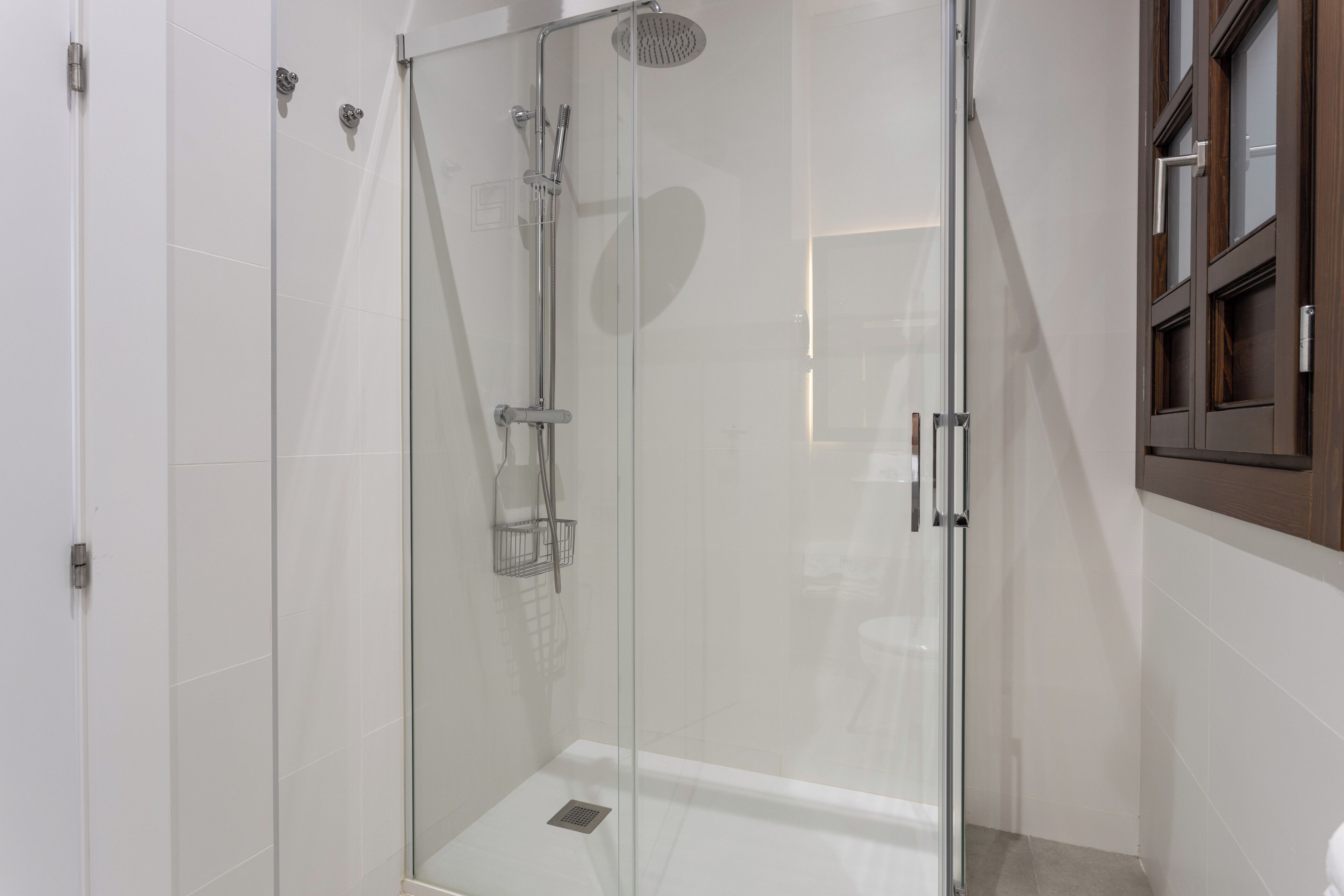 Une douche fermée par des parois en verre, dotée d’un pommeau de douche à main, d’un robinet mural et d’une petite étagère.