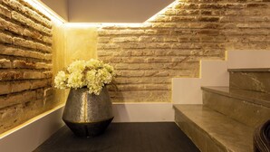 A corner with a brick wall, a metal vase with flowers, and a staircase. - BIBO SUITES PLAZA NUEVA (Granada)