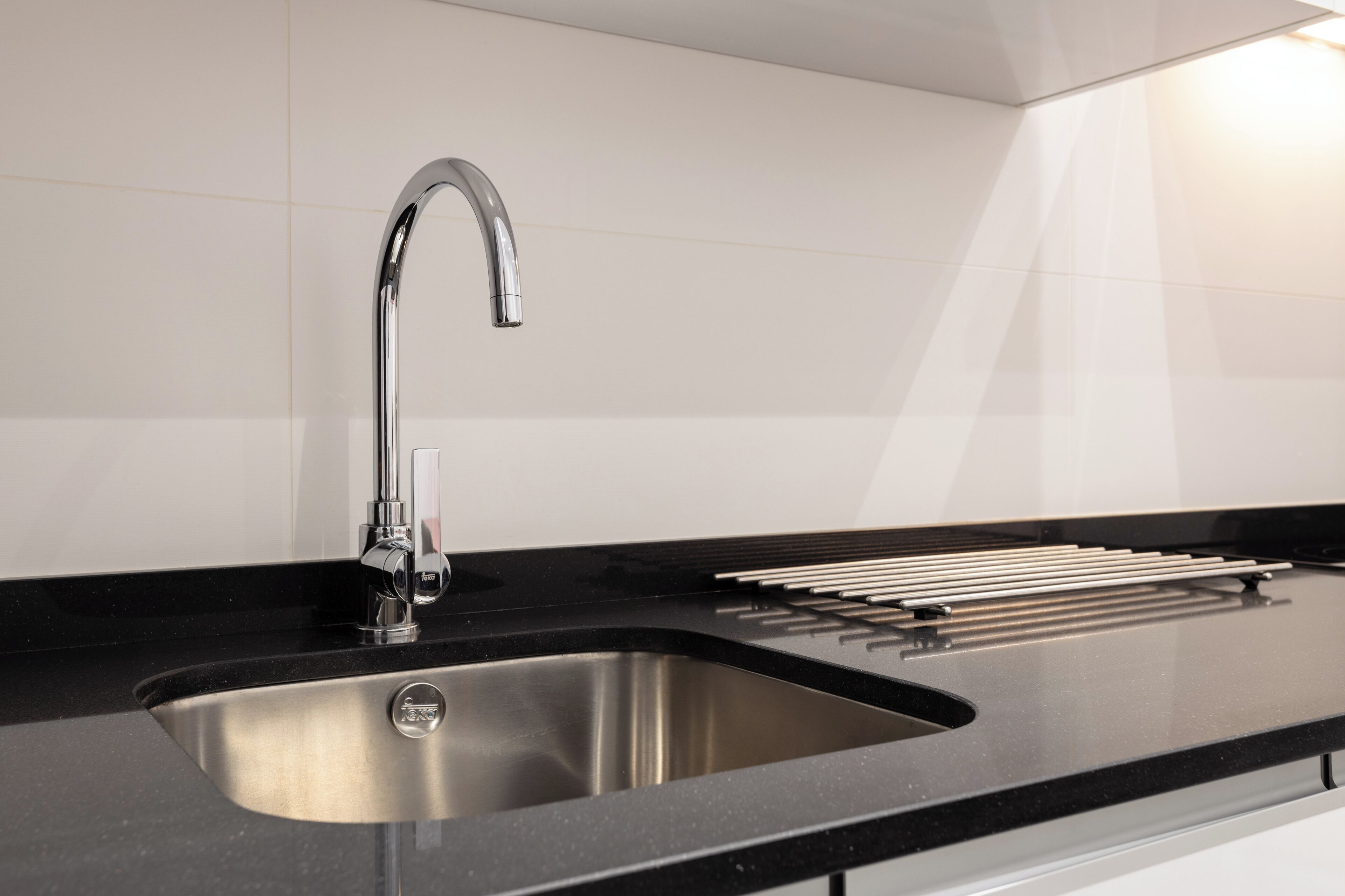 A modern kitchen with a stainless steel sink, black countertop, and a sleek faucet.