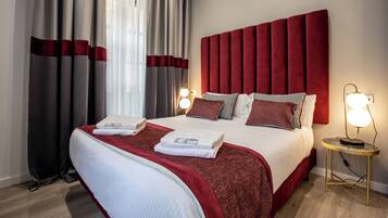 Una camera d'albergo con un letto grande, un poggiatesta rosso e due lampade da comodino.