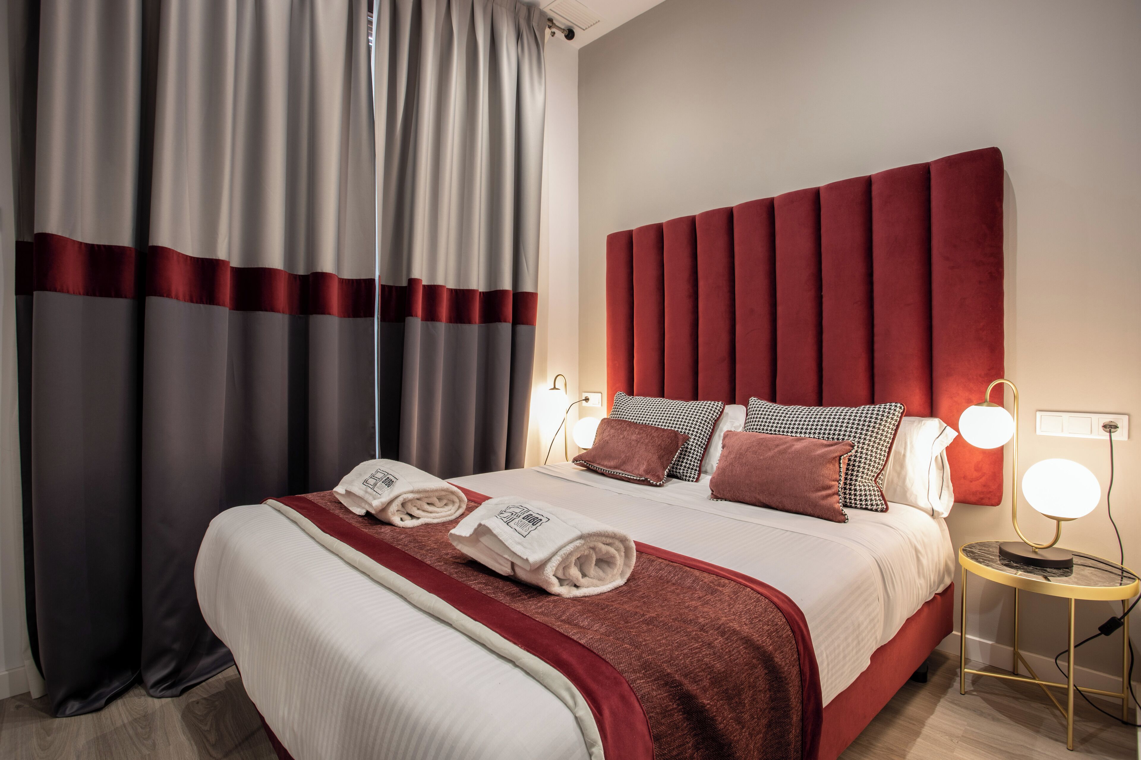 A hotel room with a large bed, red headboard, and two bedside lamps.