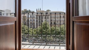 A view from a window with a wrought iron balcony railing, overlooking a row of buildings with multiple stories and balconies. - BIBO SUITES PLAZA NUEVA (Granada)