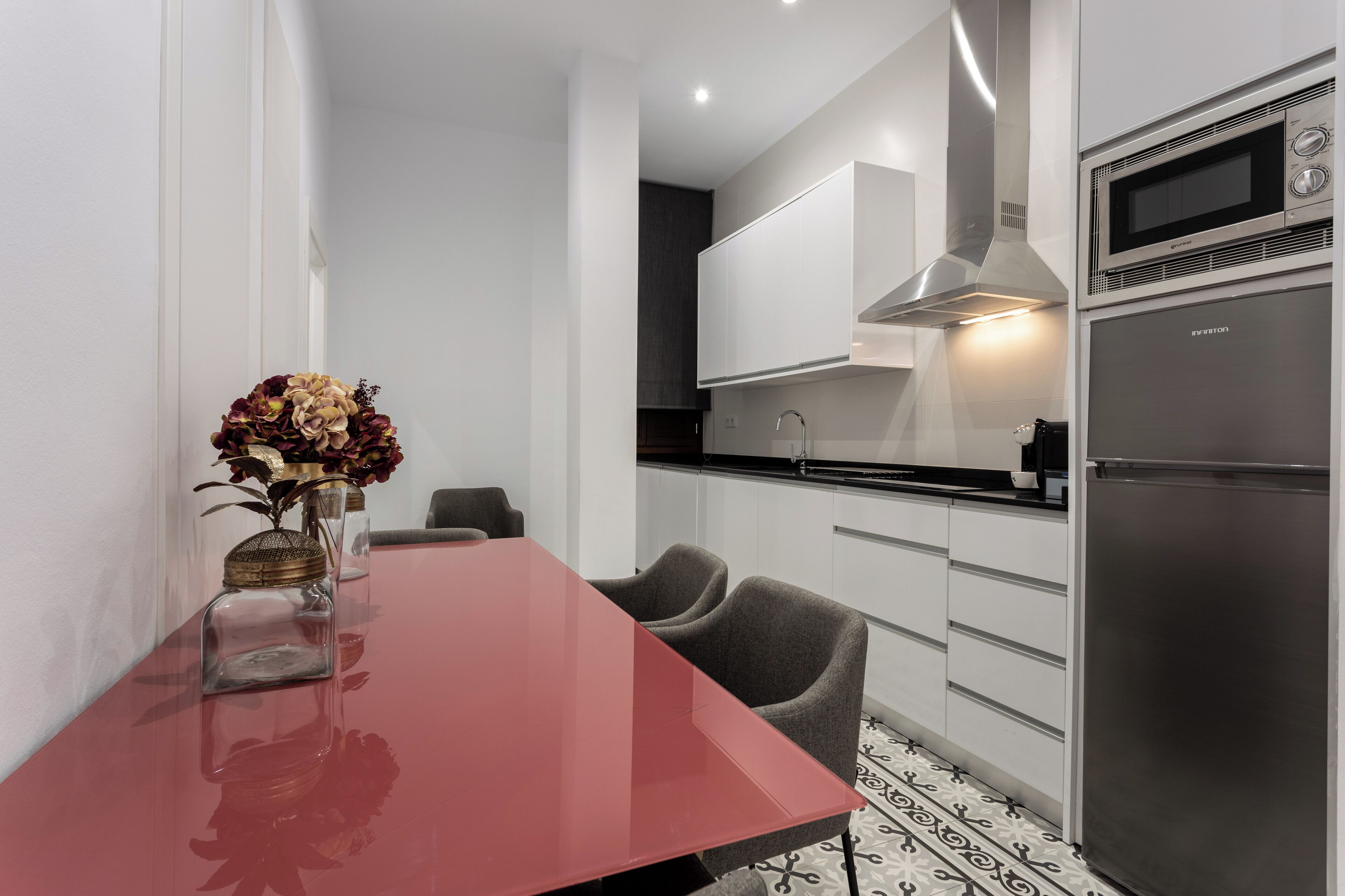 Una cocina moderna con armarios blancos, un refrigerador de acero inoxidable y un comedor rojo con sillas.
