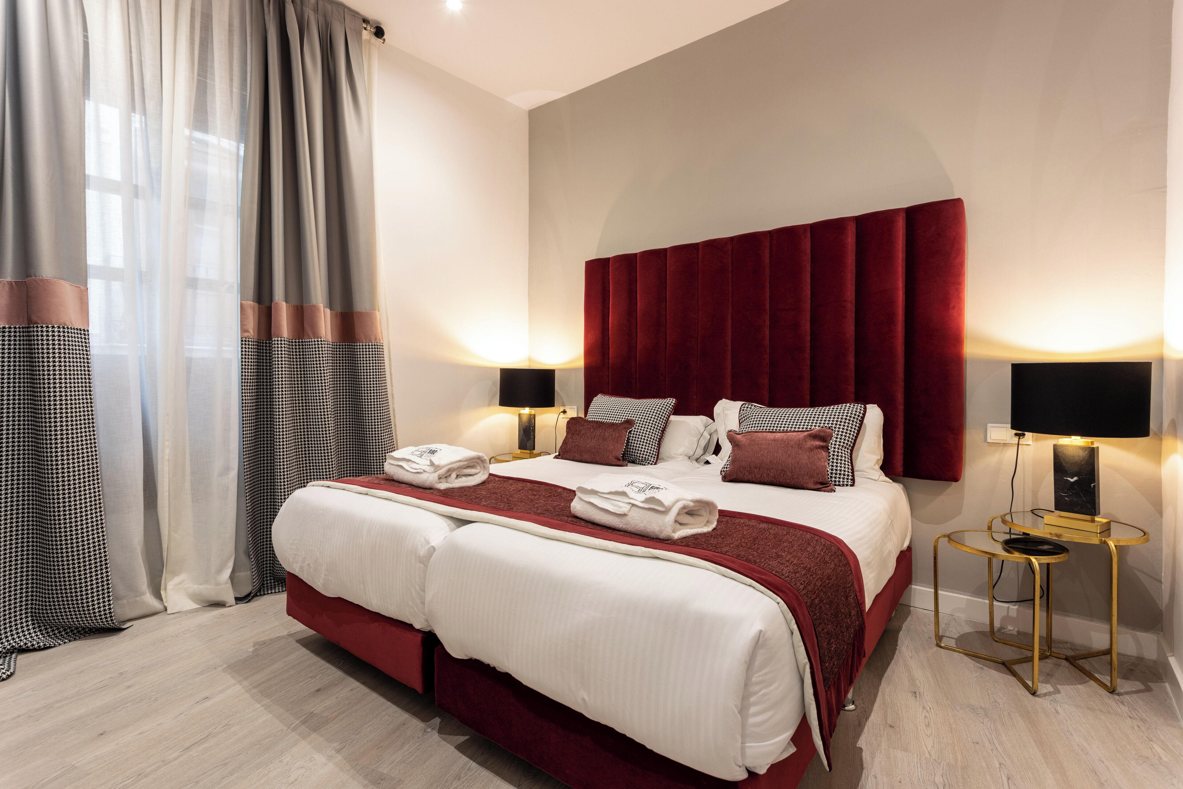 A hotel room with a large bed, two bedside tables, a red headboard, and a view of the city through the window.