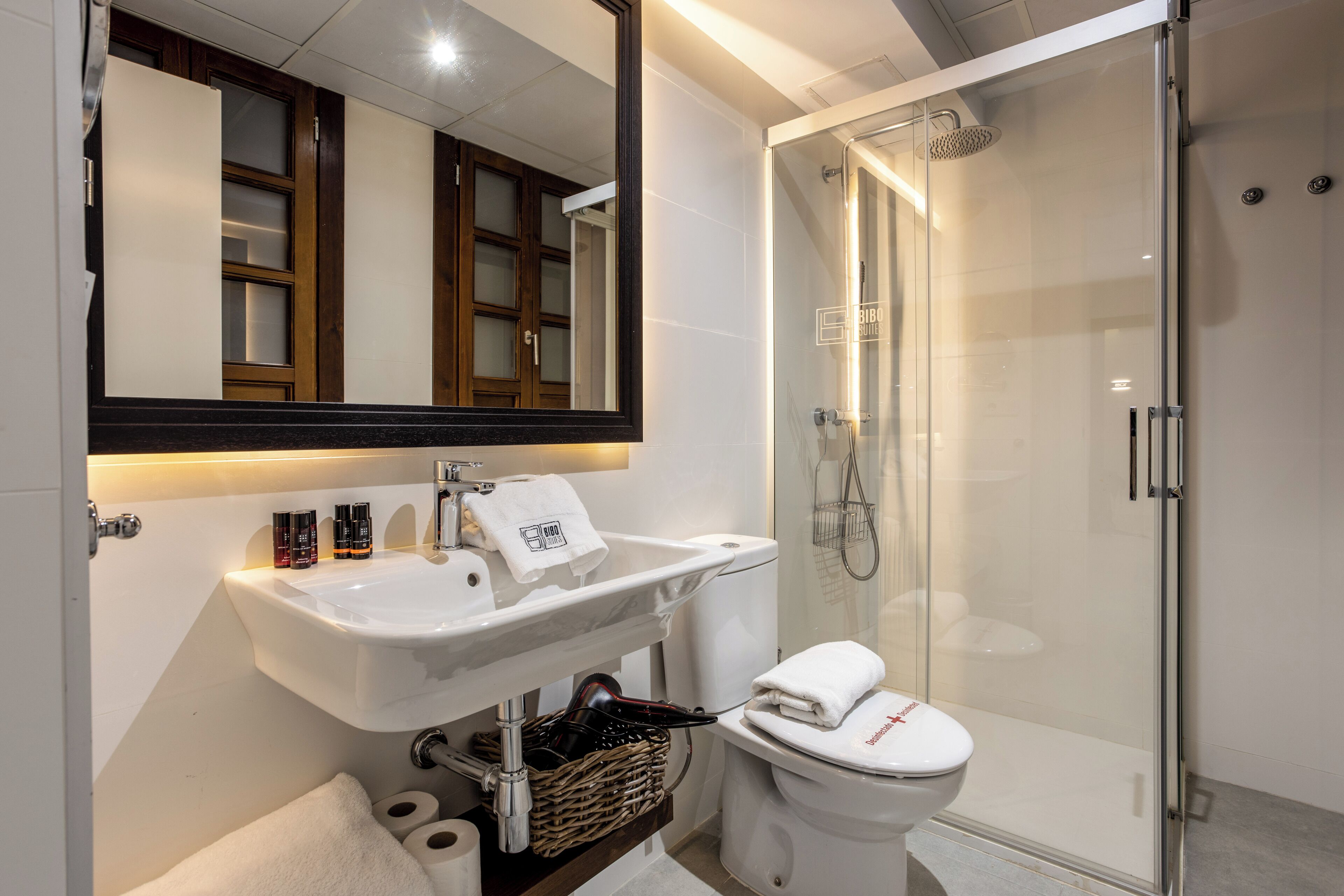 Un baño moderno con lavamanos, espejo y retrete blancos.