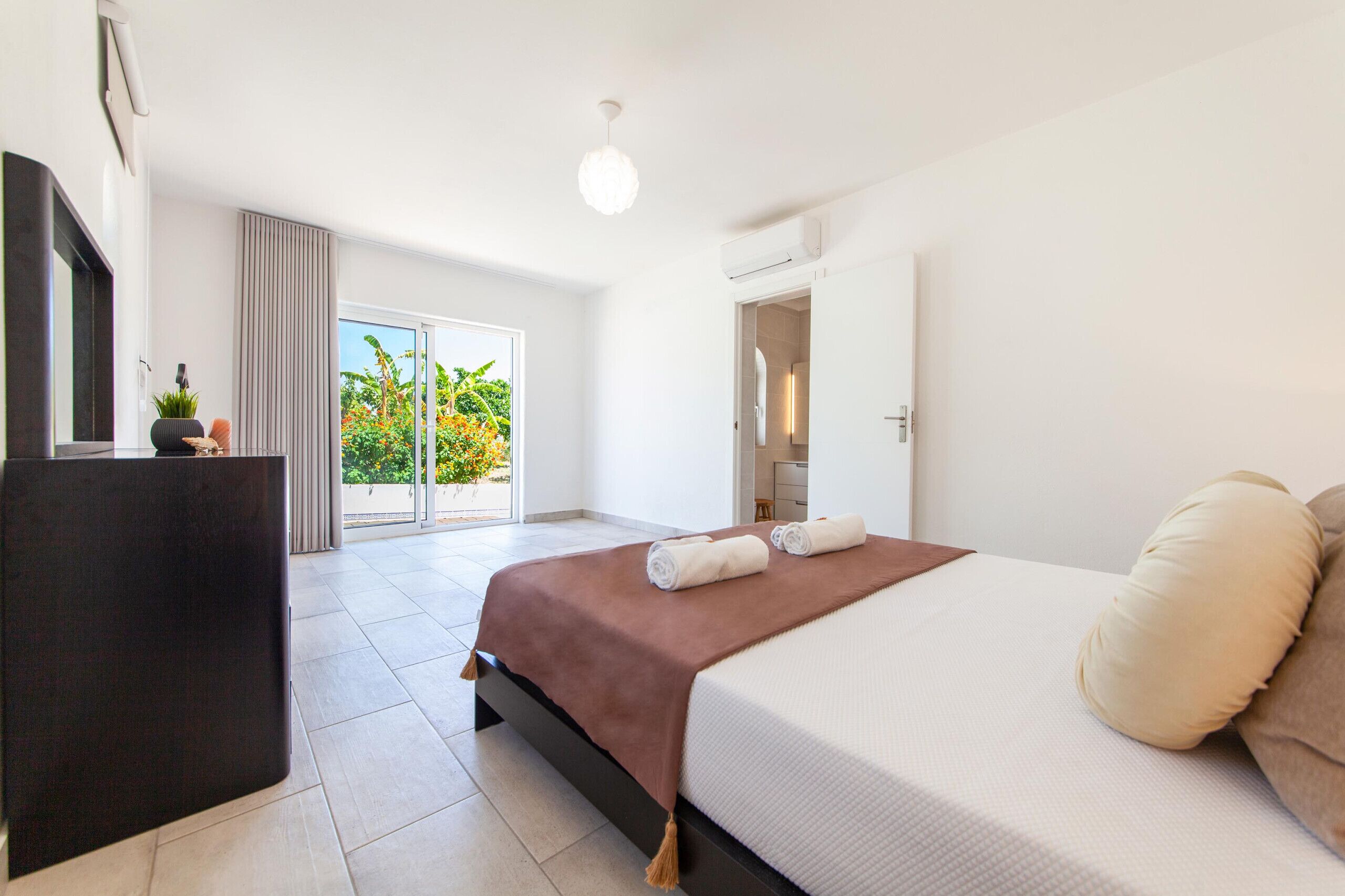 A modern hotel room with a large bed, a desk, and a view of a balcony with plants.